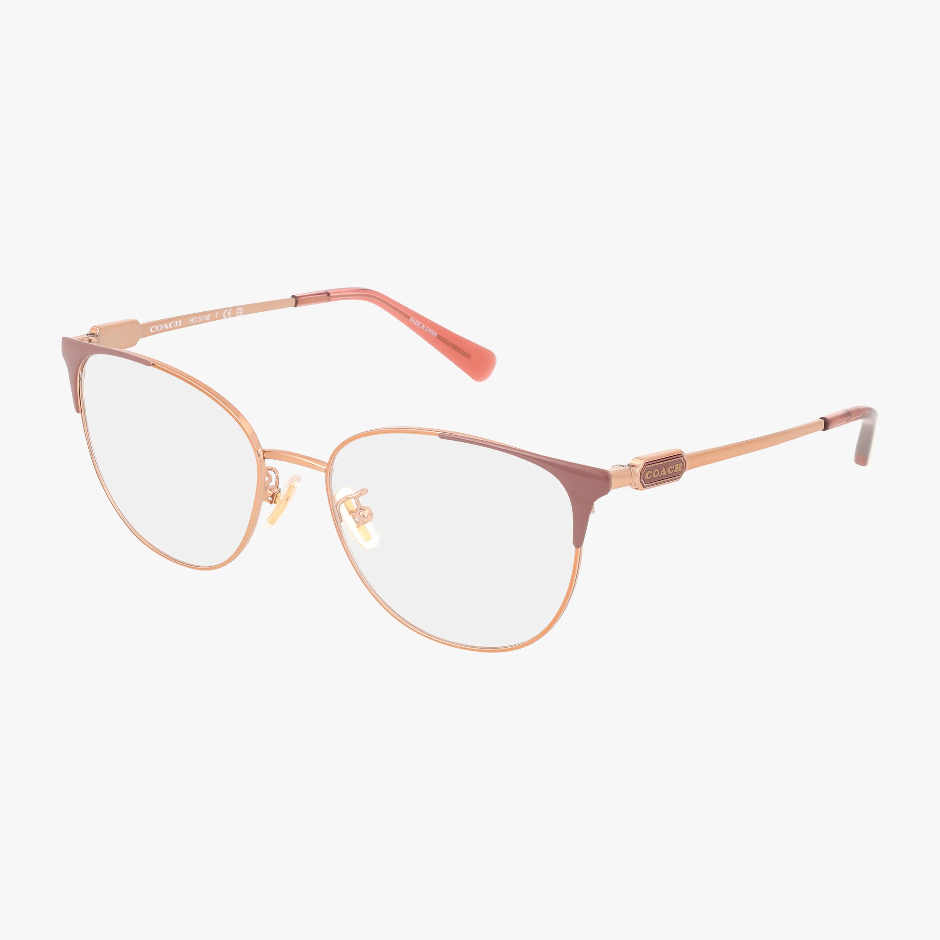 The HC5148 is a pair of stylish eyeglasses with gold metal frames, reddish-brown browline accents, and clear lenses. Delicate temples with a Coach logo near the hinges highlight its lasting resilience and timeless appeal.