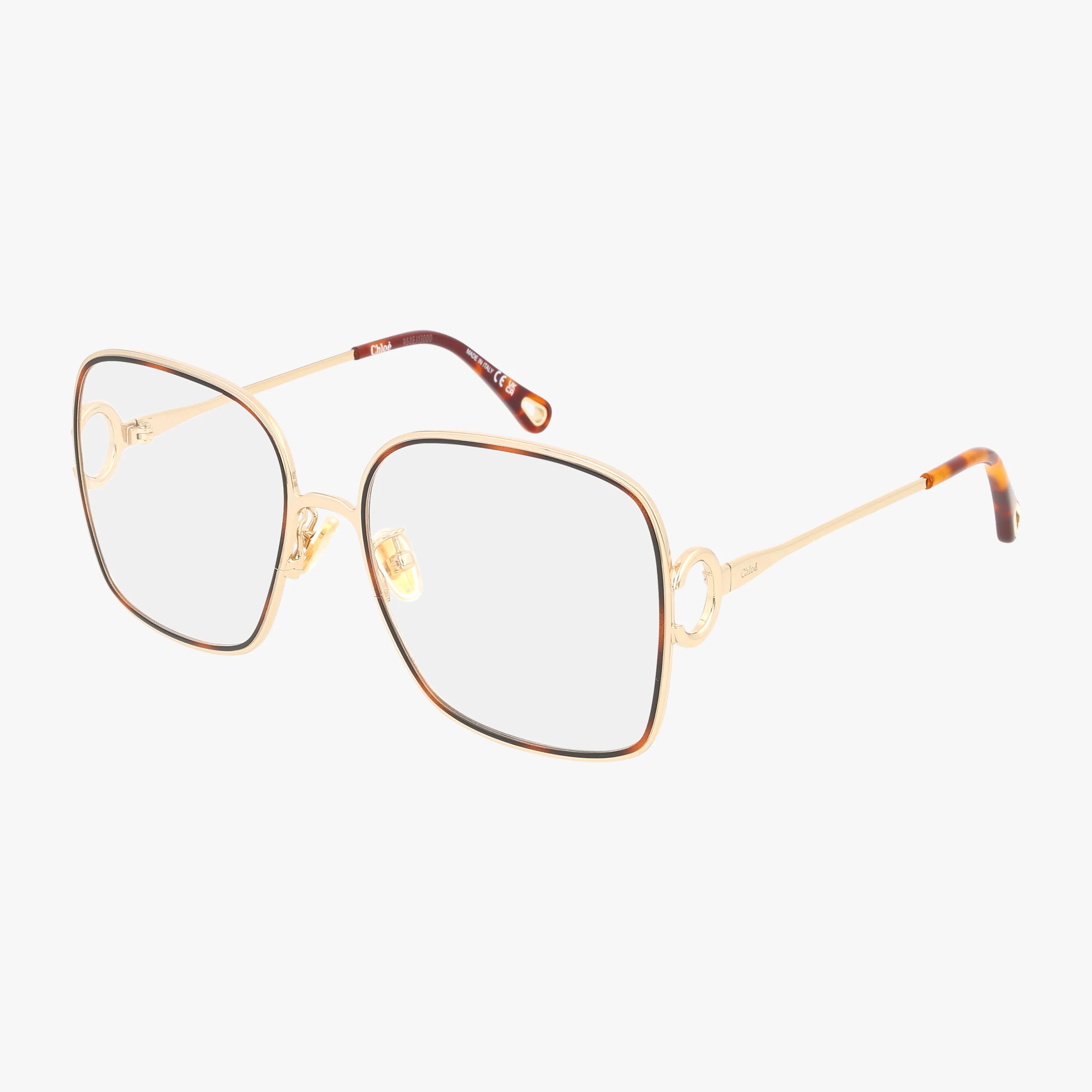The CH0147O eyeglasses feature large, square gold metal frames with clear lenses and thin arms ending in tortoiseshell tips. Crafted from modern materials, these stylish glasses are shown on a white background.